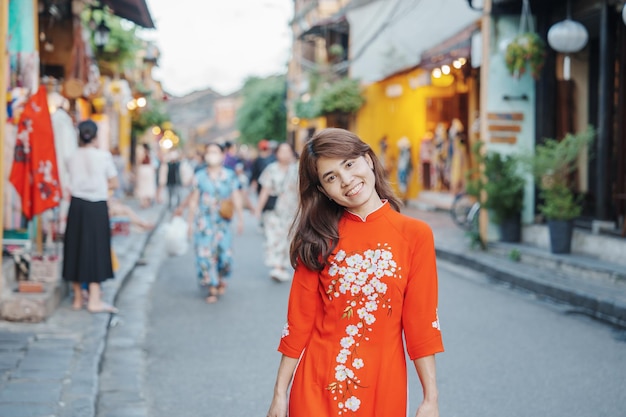 Donna felice che indossa un abito vietnamita Ao Dai viaggiatore asiatico che fa un giro turistico a Hoi An antica città nel punto di riferimento del Vietnam centrale e popolare per le attrazioni turistiche Concetto di viaggio del Vietnam e del sud-est