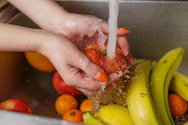 Donna felice che lava la frutta alle mele dei mandarini delle banane della cucina