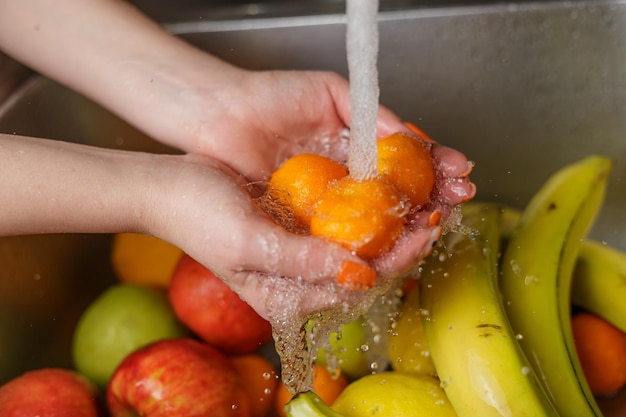 Donna felice che lava la frutta alle mele dei mandarini delle banane della cucina