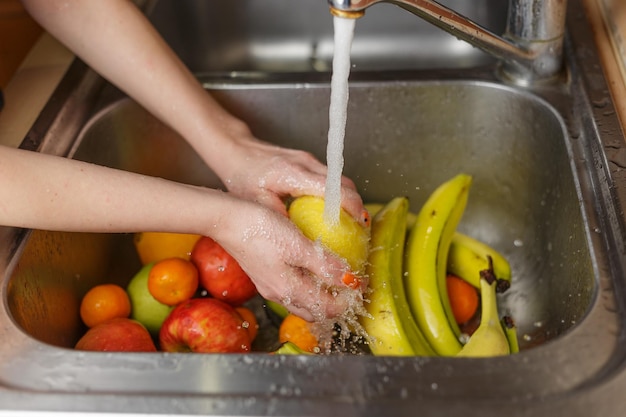 Donna felice che lava la frutta alle mele dei mandarini delle banane della cucina