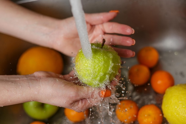 Donna felice che lava la frutta alle mele dei mandarini delle banane della cucina