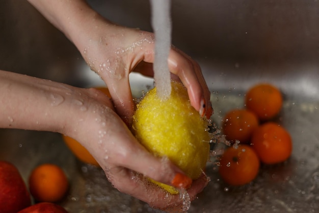 Donna felice che lava la frutta alle mele dei mandarini delle banane della cucina