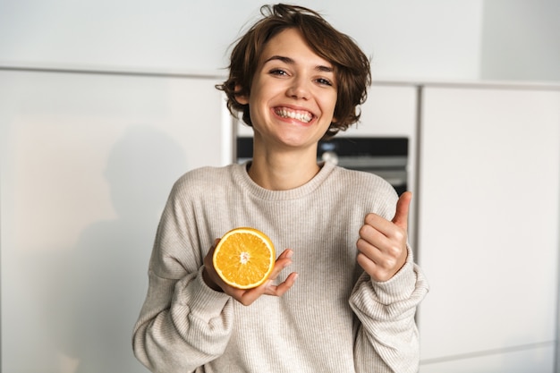 Donna felice che mostra frutta arancione mentre levandosi in piedi alla cucina