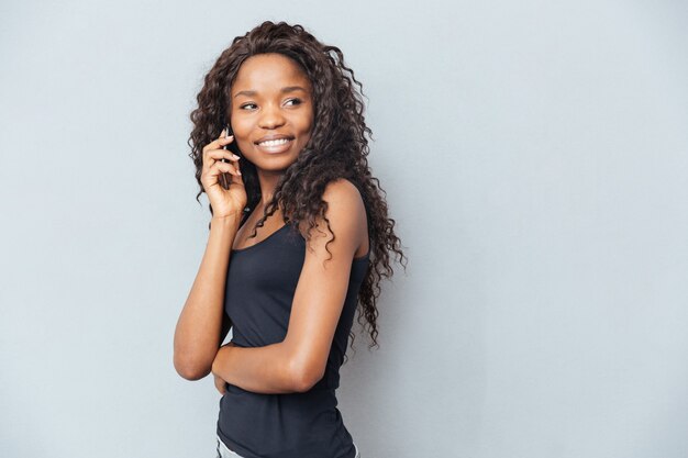 Donna felice che parla al telefono e distoglie lo sguardo oltre il muro grigio