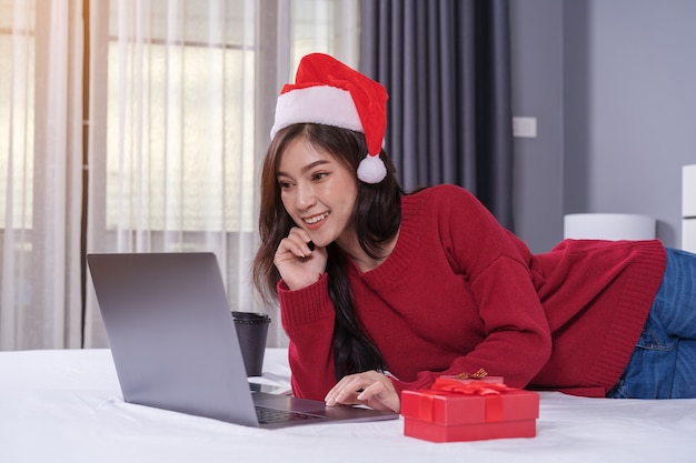 Donna felice che per mezzo del computer portatile con il regalo di Natale sul letto