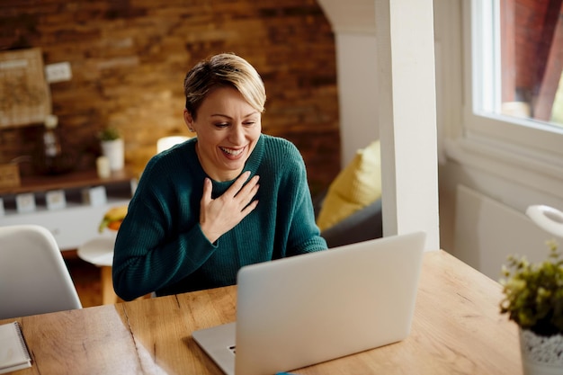 Donna felice che ride mentre fa una videochiamata sul laptop a casa