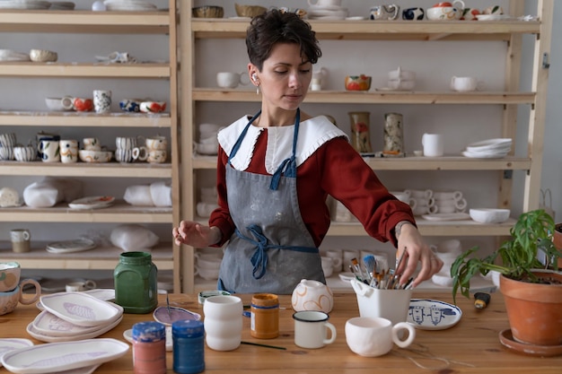 Donna felice che sceglie il pennello mentre prepara la ceramica con l'ornamento disegnato a mano carino