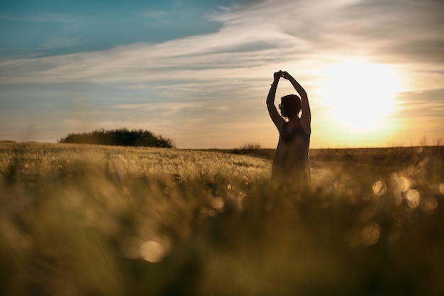 Donna felice che si gode la vita nel campo dorato, luce solare, natura meravigliosa, stile di vita all'aperto, concetto di libertà, estate, sole nel bagliore della sera.