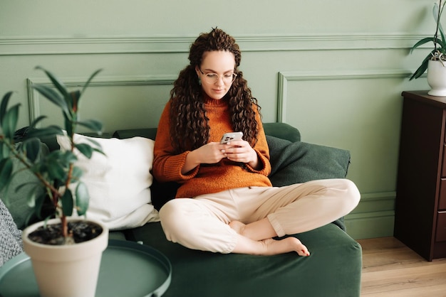 Donna felice che si rilassa sul divano utilizzando il cellulare per lo shopping e i social media a casa Concetto di e-commerce e social media