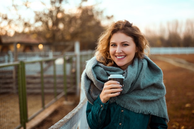 Donna felice che si scalda con caffè caldo in autunno freddo.