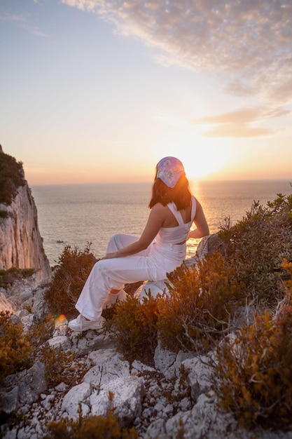 Donna felice che si siede alla vista della scogliera del faro dell'isola di Lefkada