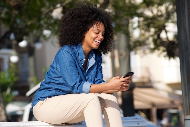 Donna felice che si siede fuori con il telefono cellulare