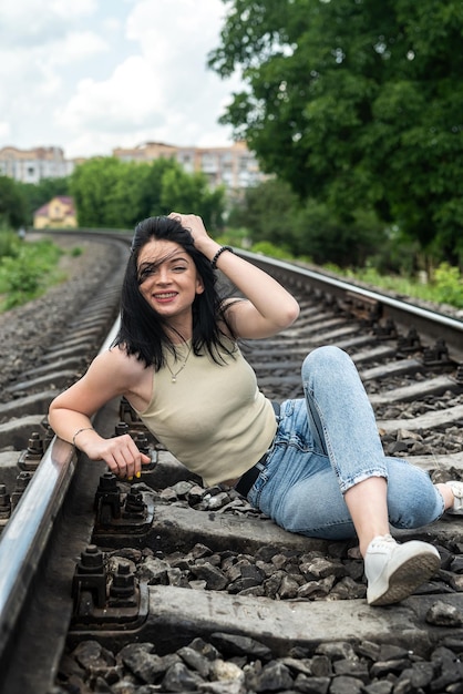 Donna felice che si siede sulla ferrovia nei binari ferroviari del panno di estate