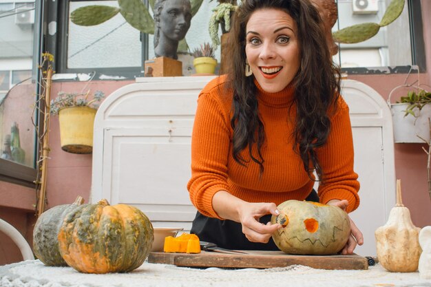 donna felice che sorride guardando la macchina fotografica mentre cava l'occhio della zucca che decora per Halloween