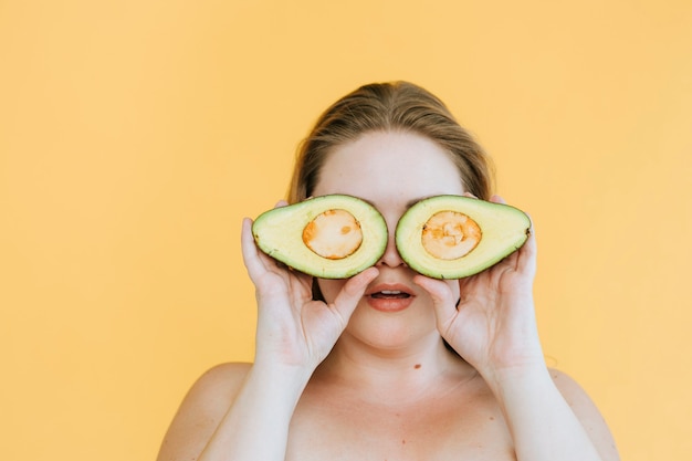 Donna felice che tiene gli avocado appena tagliati sugli occhi