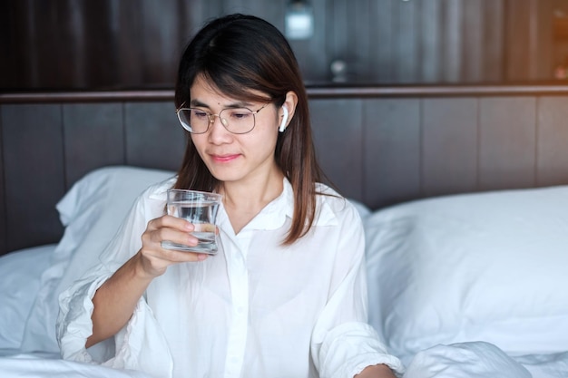 Donna felice che tiene il bicchiere d'acqua femmina che beve acqua pura sul letto a casa Concetto di stile di vita di ristoro sano