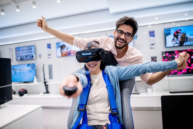 Donna felice che usando i vetri di VR e che tiene telecomando. Uomo in piedi dietro la schiena e tenendole la mano.