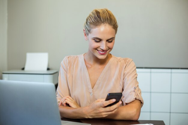 Donna felice che utilizza telefono cellulare nell'ufficio