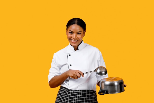 Donna felice chef nera che gioca sugli utensili da cucina divertendosi mentre cucina