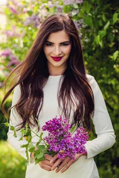 Donna felice con fiori lilla primaverili all'aperto Modello di moda ragazza bruna allegra con capelli lunghi e sani