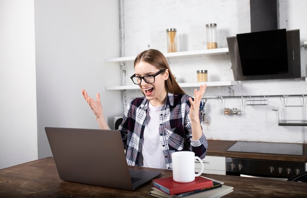 Donna felice con gli occhiali che lavorano a casa la mattina. Ragazza che beve caffè. Sta usando il suo laptop