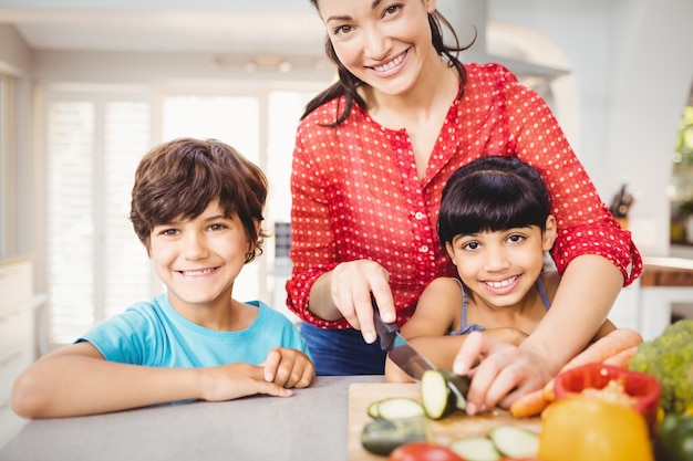 Donna felice con i bambini che tagliano le verdure a pezzi a casa