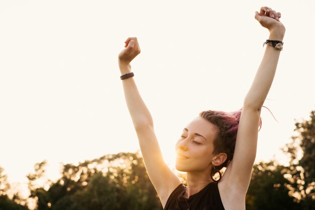 Donna felice con i dreadlocks che si allungano e inspirano aria fresca al tramonto. Ragazza piena di energia