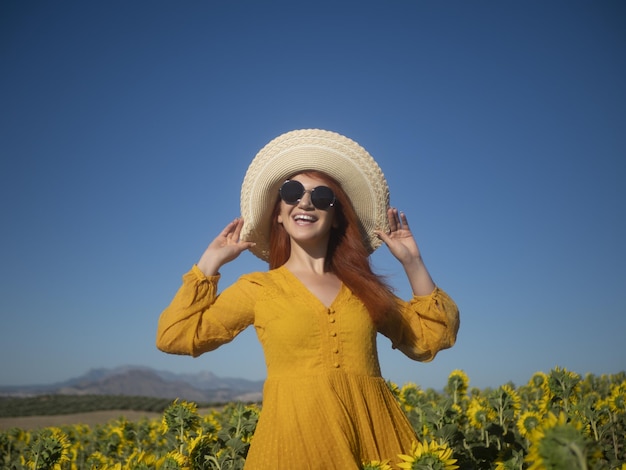 Donna felice con il cappello in piedi nel campo con i girasoli