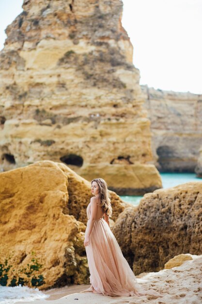 donna felice con la schiena in un vestito giallo in piedi sulla spiaggia e sul mare al tramonto