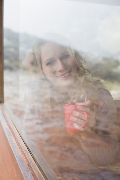 Donna felice con la tazza di caffè guardando attraverso la finestra