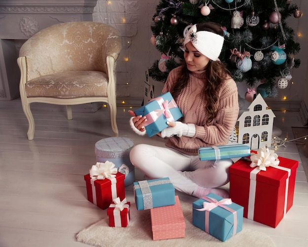 Donna felice con regali davanti all'albero di Natale Elegante donna in accogliente maglione lavorato a maglia