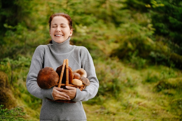 Donna felice con un cesto di funghi nel concetto di foresta di escursionismo ed ecoturismo