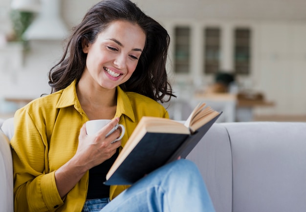 Donna felice del colpo medio con il libro e la tazza