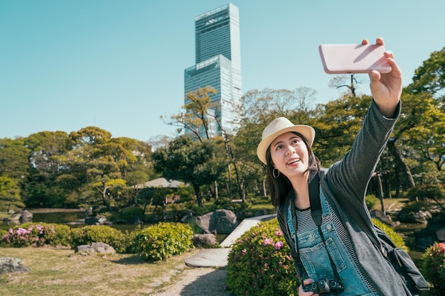 donna felice del viaggiatore che fa selfie sullo sfondo Area di Abeno ku nella città di osaka. giovane ragazza sorridente che si autoprotrait con il grattacielo sullo smartphone mentre si trova nel giardino estivo giapponese in una giornata di sole