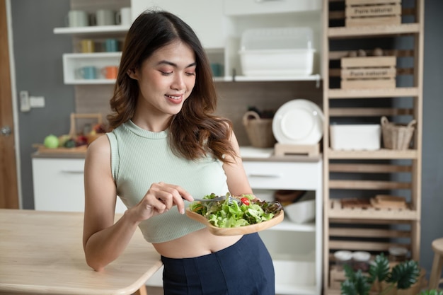 Donna felice dell'Asia che mangia insalata nella stanza della cucina