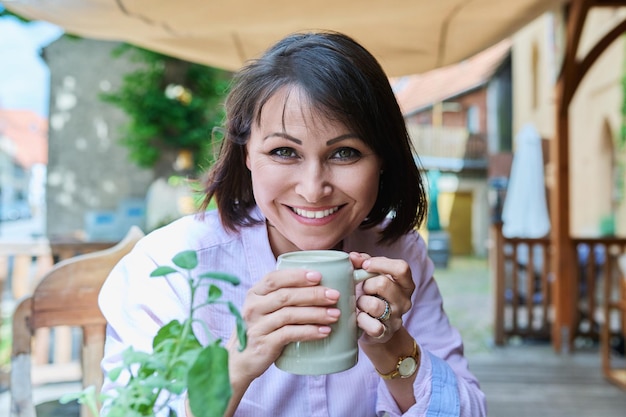 Donna felice di mezza età con boccale di birra in ceramica in un pub tedesco all'aperto guardando la macchina fotografica in una giornata di sole Cultura della birra ricreazione relax turismo tempo libero concetto di persone