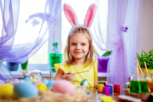 Donna felice di pasqua in orecchie del coniglietto che dipingono le uova, piccolo bambino a casa. vacanze di primavera