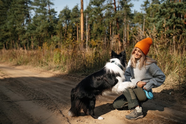 Donna felice e cane border collie bianco e nero nella foresta di autunno