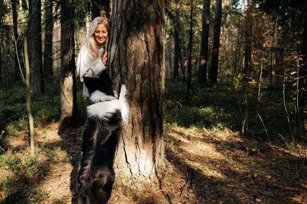 Donna felice e cane border collie bianco e nero nella foresta di autunno