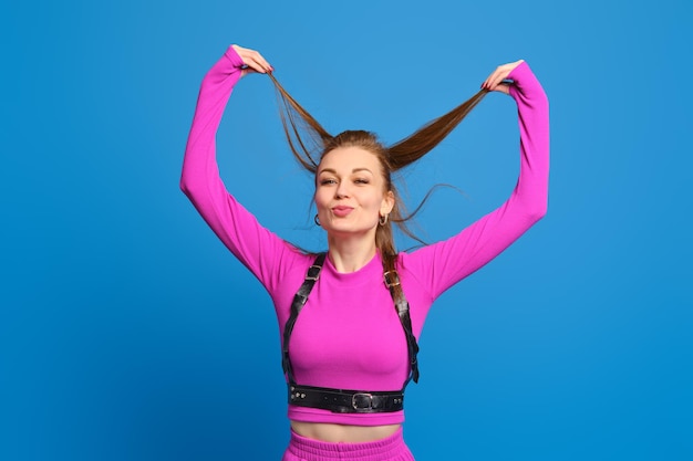 Donna felice in abito lavorato a maglia viola che gioca con i capelli su sfondo blu per studio