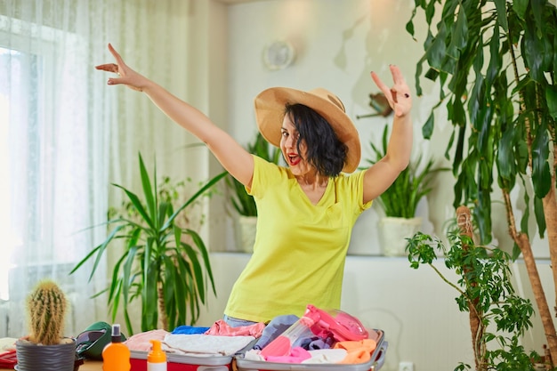 Donna felice in cappello che balla la valigia dell'imballaggio che si prepara per le vacanze estive