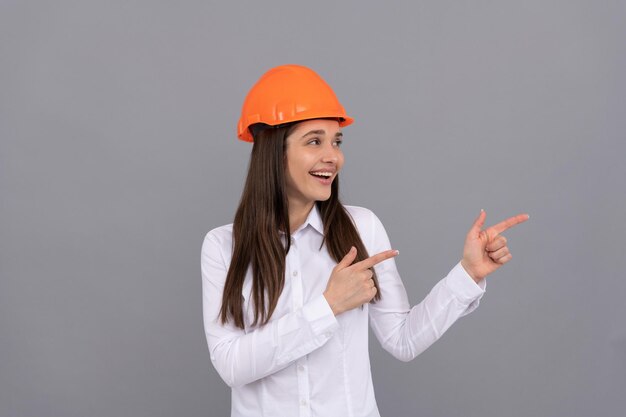 Donna felice in casco protettivo e camicia bianca che punta il dito da parte per dirigere