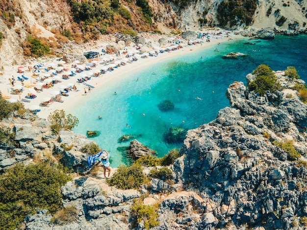 Donna felice in costume da bagno blu che tiene la bandiera della Grecia in cima alla scogliera