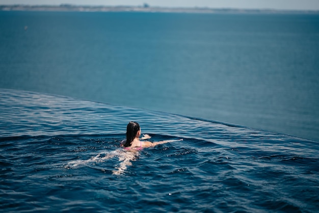 Donna felice in costume da bagno che nuota nella piscina a sfioro contro il lungomare