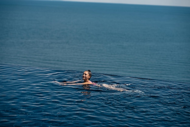 Donna felice in costume da bagno che nuota nella piscina a sfioro contro il lungomare