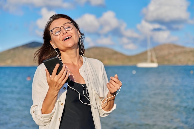 Donna felice in cuffia che ascolta musica utilizzando lo smartphone sulla spiaggia