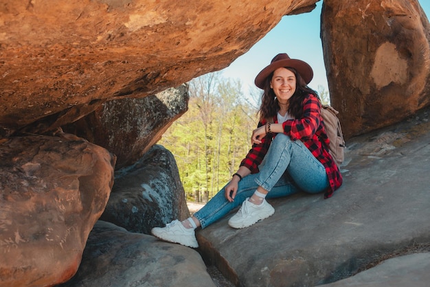 Donna felice in jeans e cappello escursionista seduto alla roccia