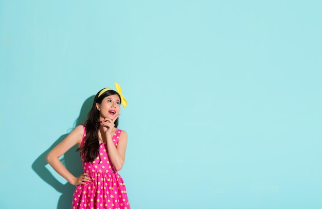 donna felice in piedi sullo sfondo blu guardando l'attrattiva del contenuto pubblicitario vuoto copyspace e mostrando il gesto del dito puntato sul viso che indossa un bel vestito.