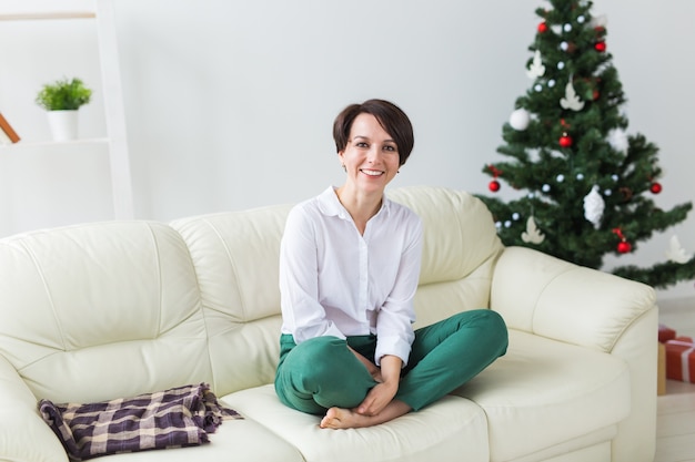 Donna felice in posa sul divano accanto all'albero di Natale