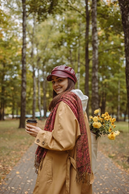 donna felice in trincea con borsa di fiori e tazza di caffè per andare